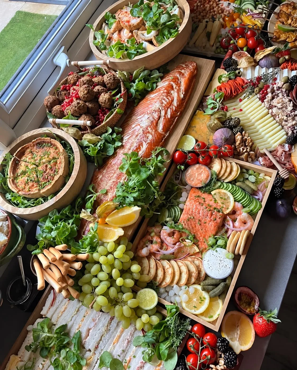 A generous grazing table with salmon, cheeses, quiche, salad and fresh fruit